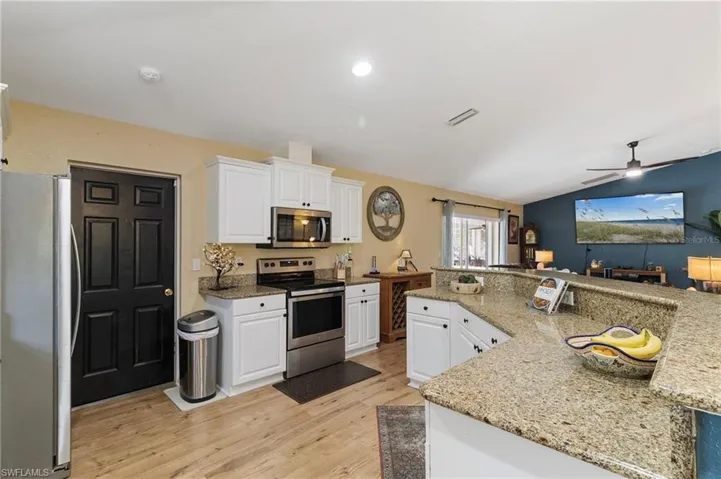 Kitchen with stainless steel appliances, white cabinets, a ceiling fan, a center island, and vaulted ceiling