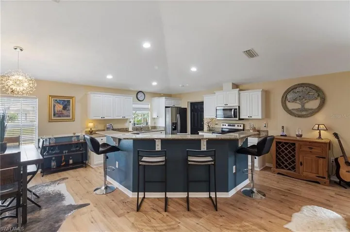 Two tone kitchen with a breakfast bar area, a chandelier, stainless steel appliances, light wood-style flooring, and dark stone countertops