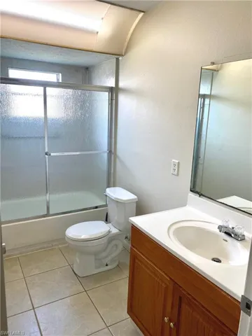 Full bath with vanity, light tile patterned floors, bath / shower combo with glass door, and a textured wall