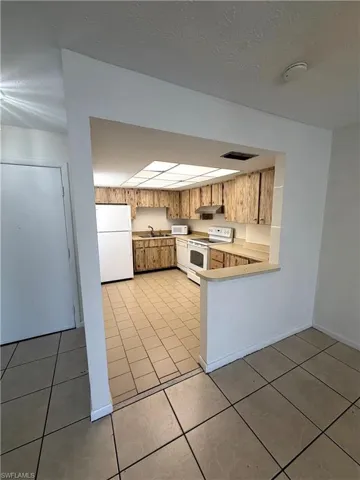 Kitchen with light countertops, white appliances, a peninsula, a textured ceiling, and light tile patterned flooring