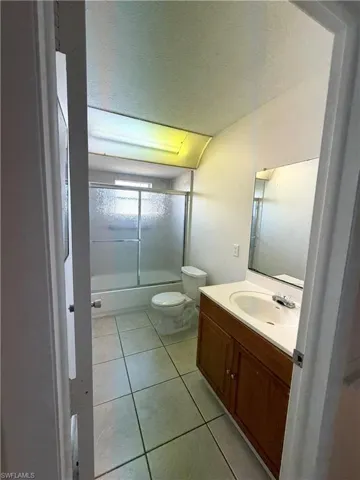 Bathroom featuring a textured ceiling, light tile patterned floors, enclosed tub / shower combo, and vanity