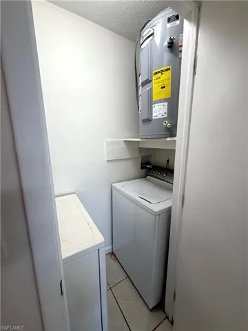 Laundry room with light tile patterned floors, a textured ceiling, water heater, and washing machine and clothes dryer