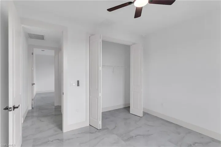 Unfurnished bedroom with light marble finish floors, a closet, and a ceiling fan