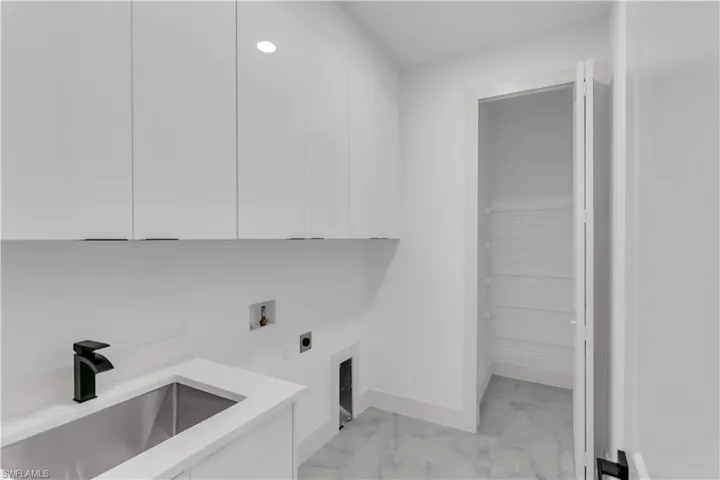 Laundry area with hookup for an electric dryer, hookup for a washing machine, light marble finish flooring, and cabinet space