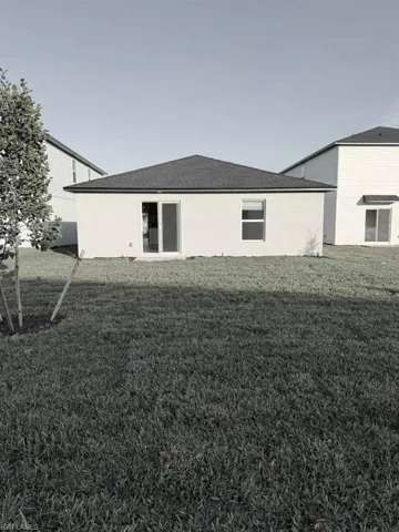 Back of property with a yard, stucco siding, and a shingled roof