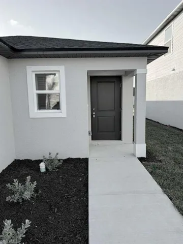 View of exterior entry featuring a shingled roof and stucco siding