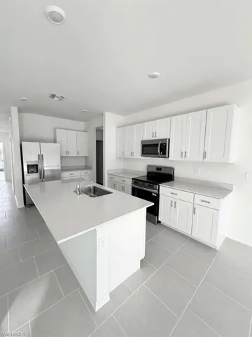 Kitchen featuring stainless steel appliances, white cabinetry, a center island with sink, and light tile patterned floors