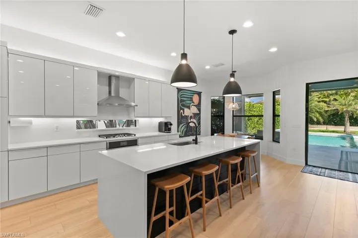 Kitchen with a sink, light wood-style flooring, wall chimney exhaust hood, and modern cabinets