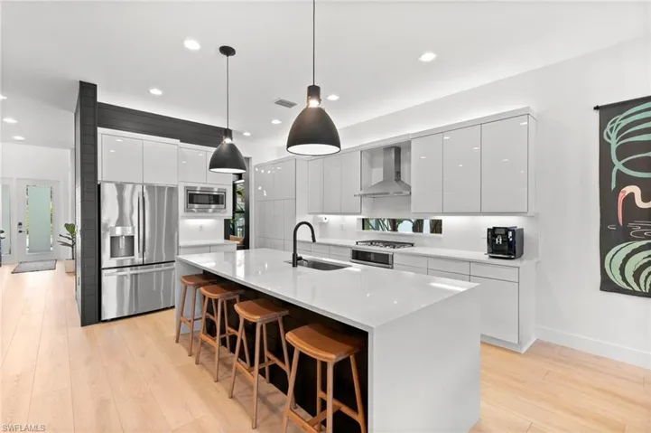 Kitchen with modern cabinets, a sink, wall chimney range hood, appliances with stainless steel finishes, and a breakfast bar
