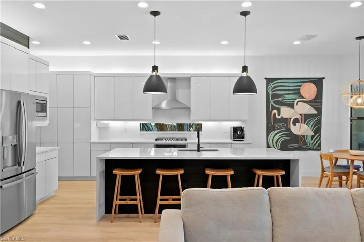 Kitchen with a breakfast bar, wall chimney exhaust hood, modern cabinets, and stainless steel appliances