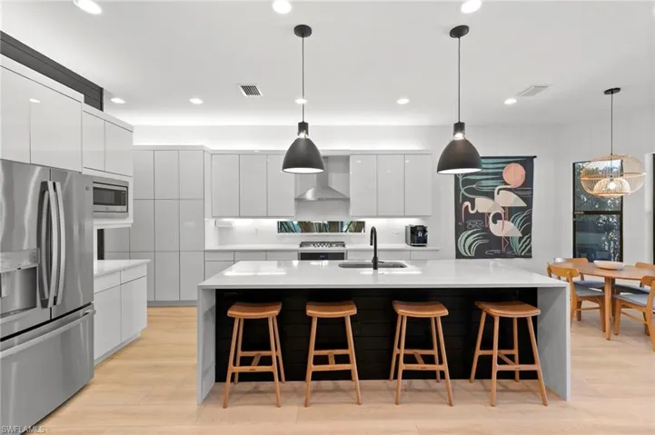 Kitchen featuring visible vents, wall chimney exhaust hood, modern cabinets, appliances with stainless steel finishes, and a sink