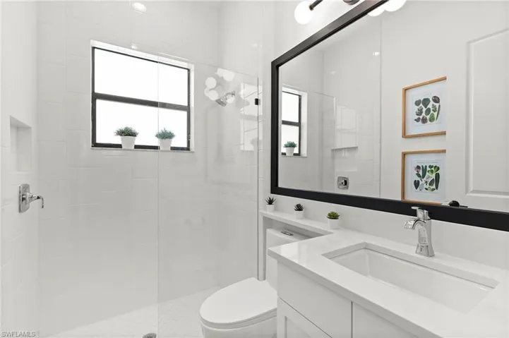 Bathroom with tiled shower, vanity, plenty of natural light, and toilet