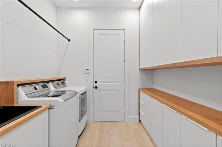 Laundry area with independent washer and dryer, light wood-type flooring, and cabinet space