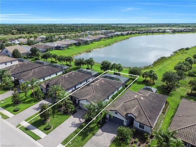 Waterfront property featuring a paver driveway, lush landscaping, and an enclosed pool