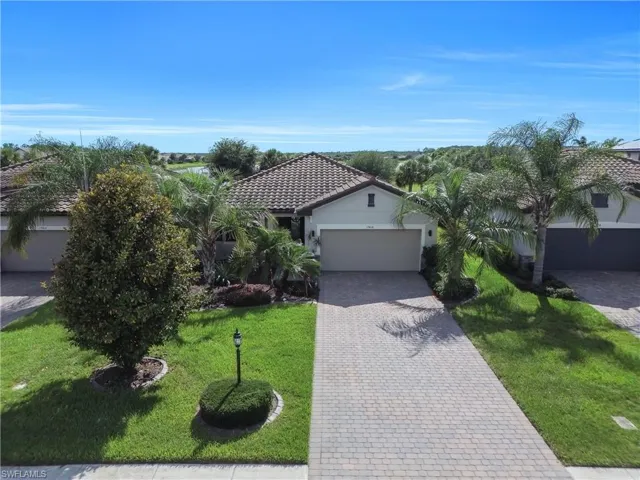 Tiled roof residence featuring an attached garage, paver driveway, and mature landscaping