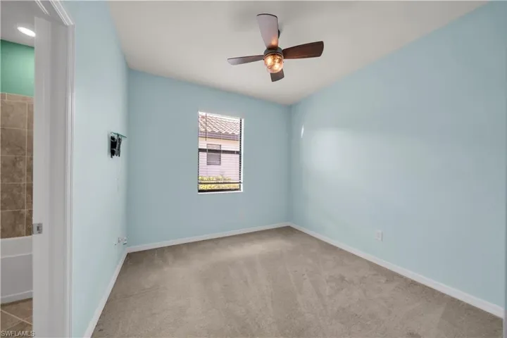 Textured carpeting, window with blinds, ceiling fan with light fixture, and light blue wall finish