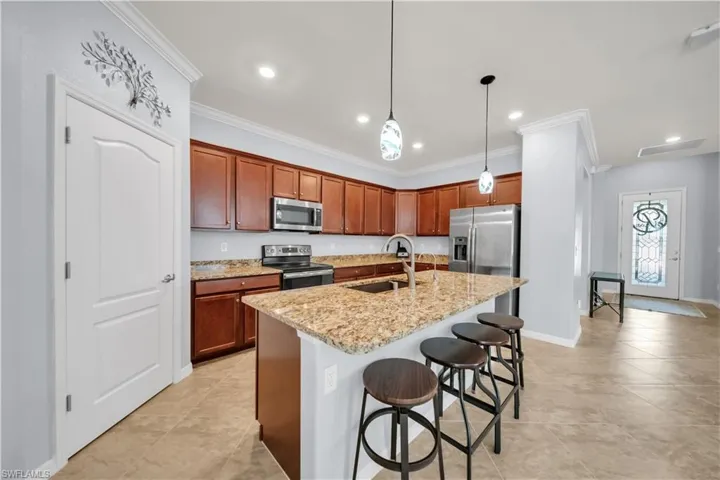 Kitchen featuring wood cabinetry, stainless steel appliances, a multi-level island with seating, pendant lighting, and tiled flooring