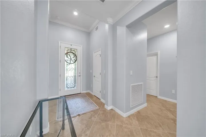 Entryway with a decorative glass-paneled front door, recessed lighting, crown molding, and large format tile flooring