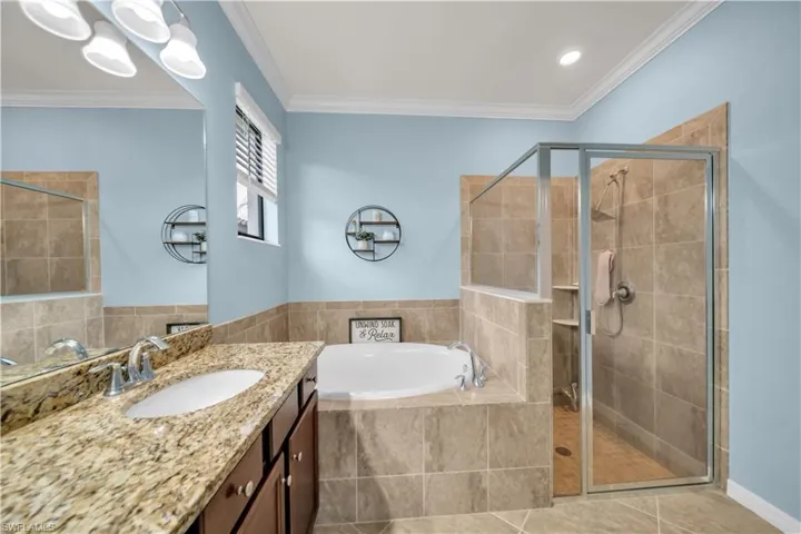 Bathroom featuring an enclosed glass shower, a built-in soaking tub, a single vanity with an undermount sink, and a stone-finish countertop