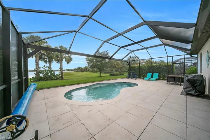 Screened outdoor living area featuring a freeform swimming pool, spacious patio, and water frontage