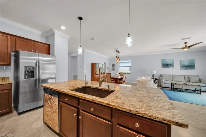 Kitchen island with stone countertop, stainless steel appliances, pendant lighting, wood cabinetry, and tile flooring