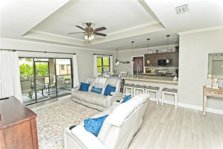 Living area with a raised ceiling, light wood-style floors, crown molding, and a ceiling fan