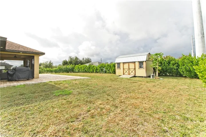 View of grassy yard featuring a patio area, a storage unit, and a ceiling fan