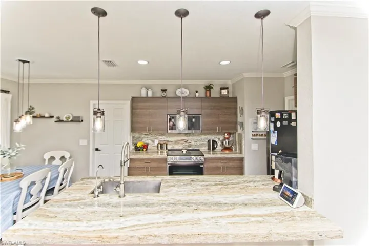 Kitchen with crown molding, stainless steel appliances, decorative light fixtures, light stone countertops, and backsplash