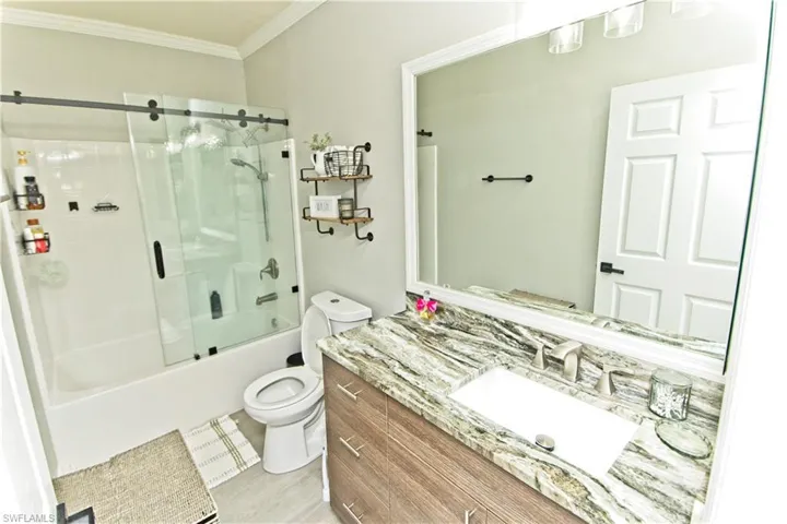 Bathroom with vanity, shower / bath combination with glass door, crown molding, and light wood-style floors