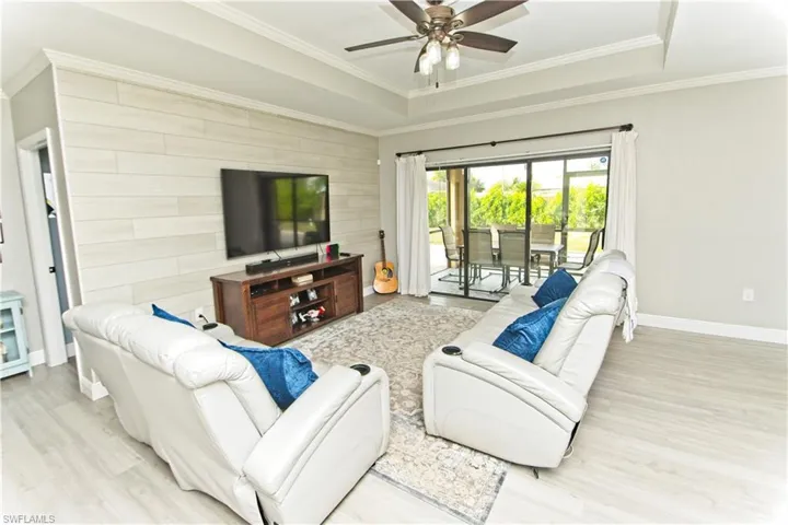 Living area featuring an accent wall, light wood finished floors, a tray ceiling, a ceiling fan, and crown molding