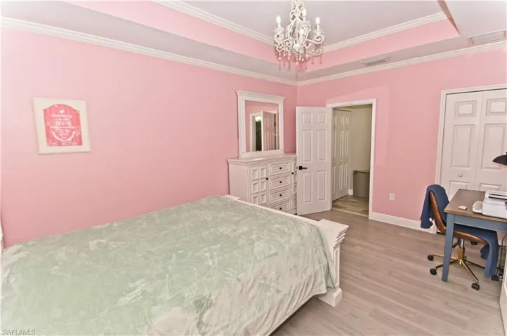 Bedroom featuring a tray ceiling, a desk, light wood-type flooring, crown molding, and a chandelier