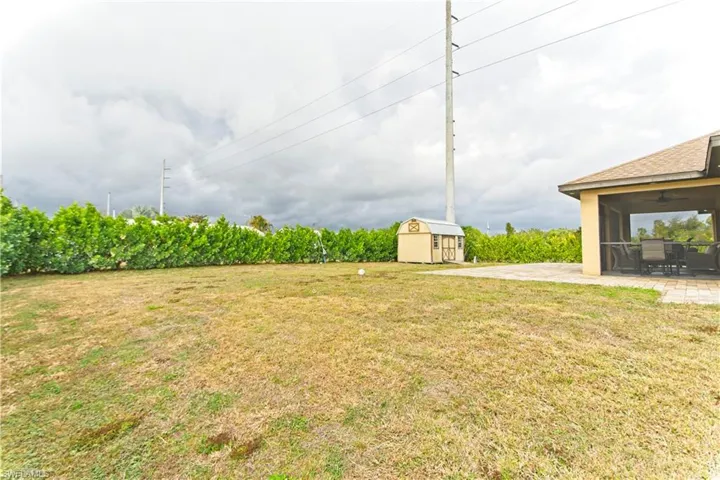 View of green lawn featuring a sunroom, a ceiling fan, a storage shed, and a patio