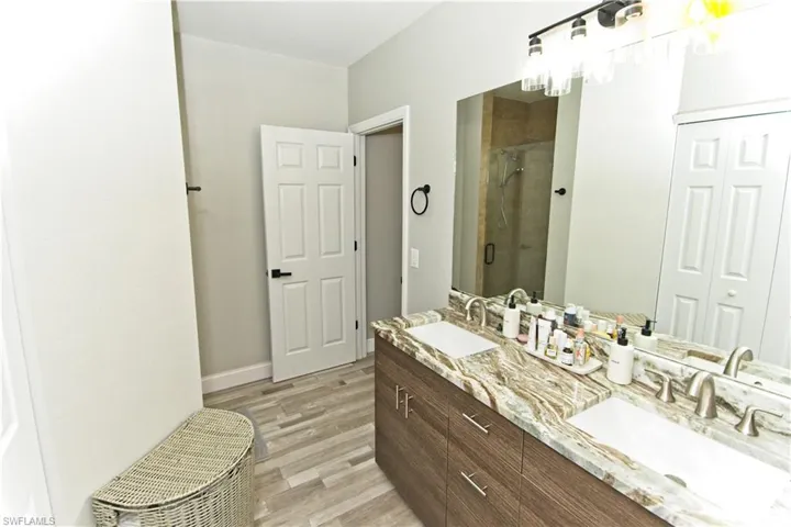 Full bathroom featuring a shower stall, double vanity, and light wood-style flooring