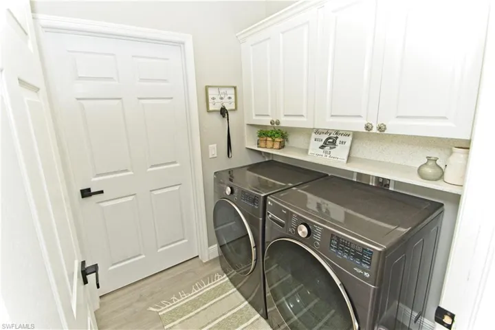 Laundry room with washing machine and clothes dryer, light wood-style flooring, and cabinet space