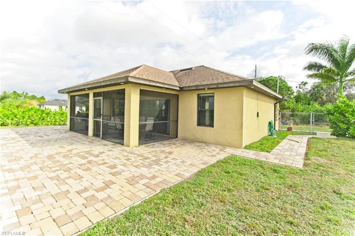 Rear view of house featuring a patio area, a shingled roof, stucco siding, a gate, and a sunroom