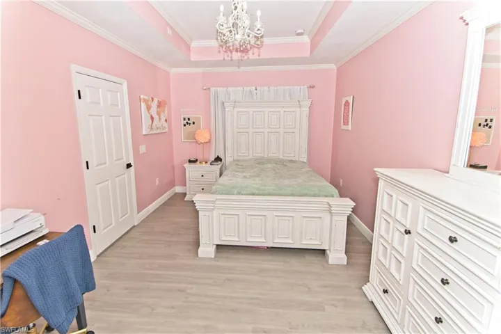 Bedroom featuring crown molding, a raised ceiling, light wood-style floors, and a chandelier