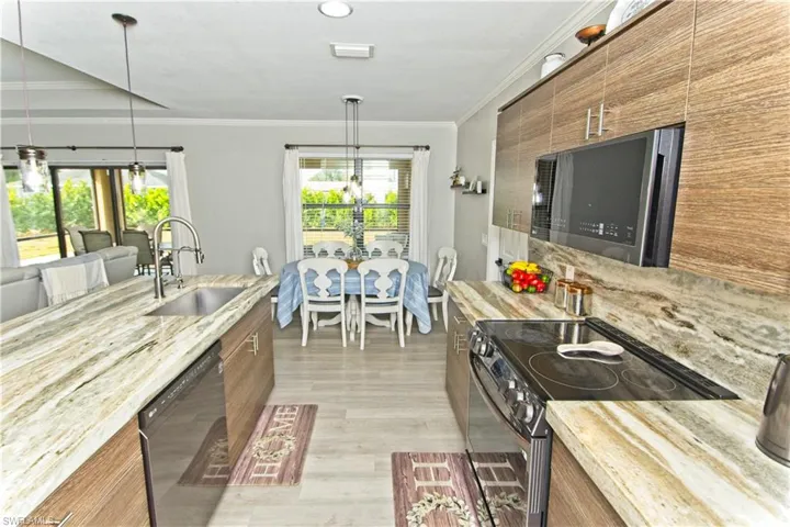 Kitchen featuring electric stove, stainless steel microwave, modern cabinets, pendant lighting, and light stone counters