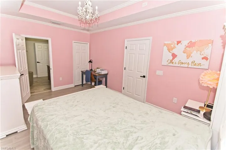 Bedroom featuring a raised ceiling, a chandelier, ornamental molding, wood finished floors, and a closet