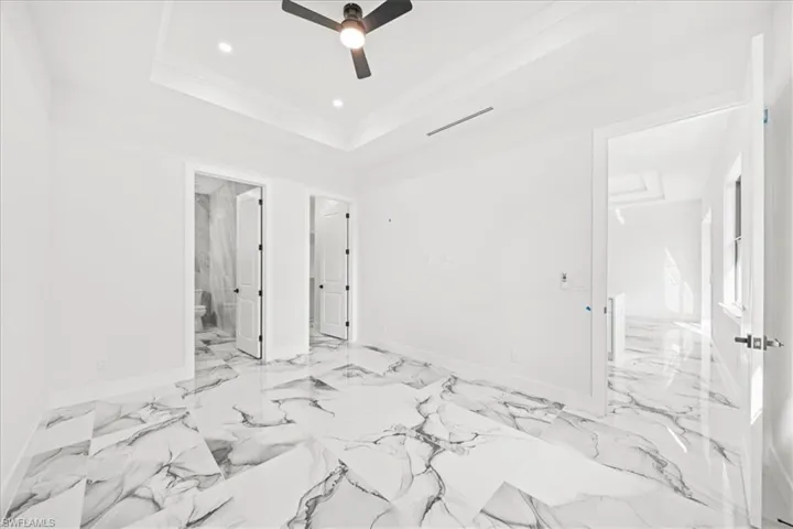 Unfurnished bedroom with ensuite bath, ceiling fan, recessed lighting, a tray ceiling, and ornamental molding