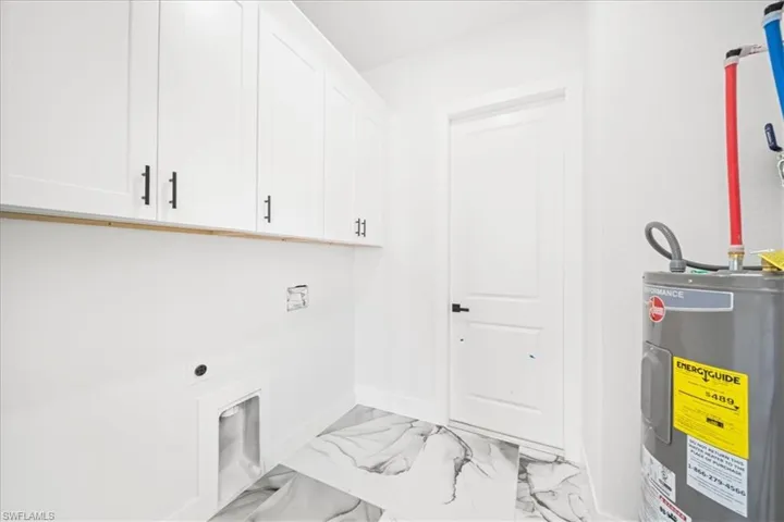 Laundry area with electric water heater, hookup for an electric dryer, cabinet space, and light marble finish floors