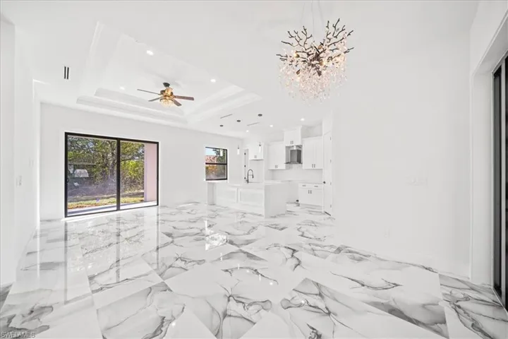 Unfurnished living room with ceiling fan, suspended lighting, and light marble finish flooring
