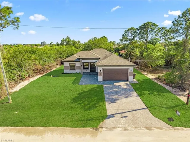 View of front of house with a front yard, driveway, a garage, roof with shingles, and stucco siding