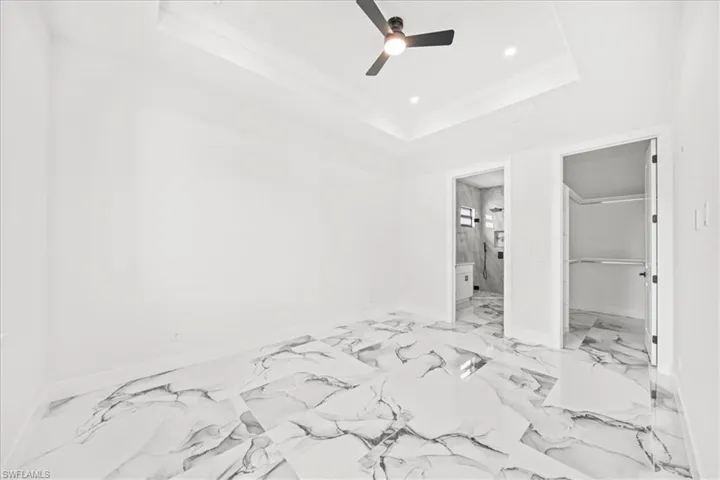 Unfurnished bedroom with a spacious closet, ceiling fan, ornamental molding, recessed lighting, and light marble finish flooring