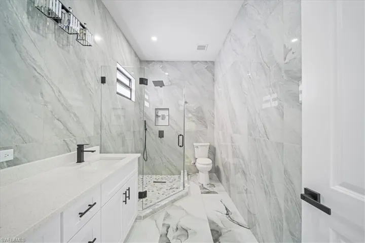 Full bathroom featuring vanity, tile walls, a marble finish shower, recessed lighting, and light marble finish flooring
