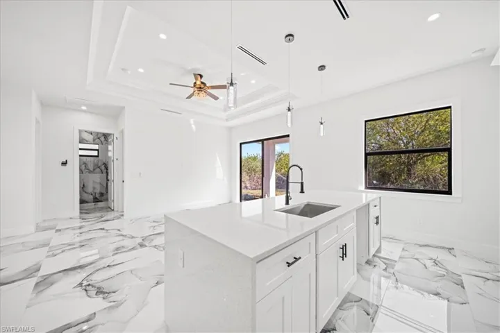 Kitchen with light stone countertops, white cabinetry, a center island with sink, hanging light fixtures, and ceiling fan