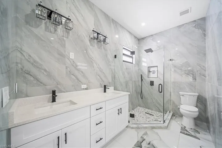 Bathroom featuring tile walls, a marble finish shower, double vanity, light marble finish floors, and recessed lighting