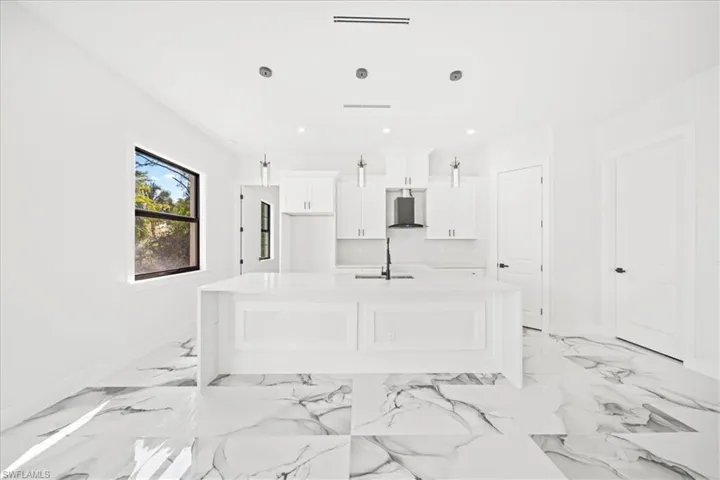 Kitchen featuring an island with sink, white cabinets, light stone countertops, and hanging light fixtures