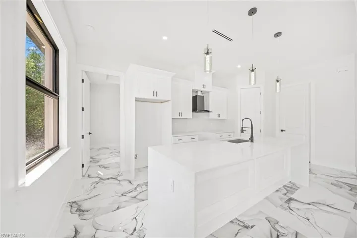 Kitchen featuring white cabinetry, an island with sink, light stone counters, hanging light fixtures, and a kitchen breakfast bar