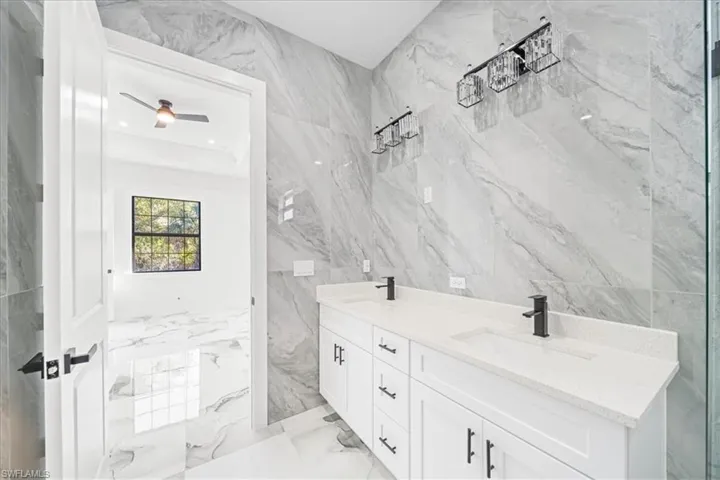 Bathroom featuring double vanity, tile walls, light marble finish flooring, ceiling fan, and stone wall