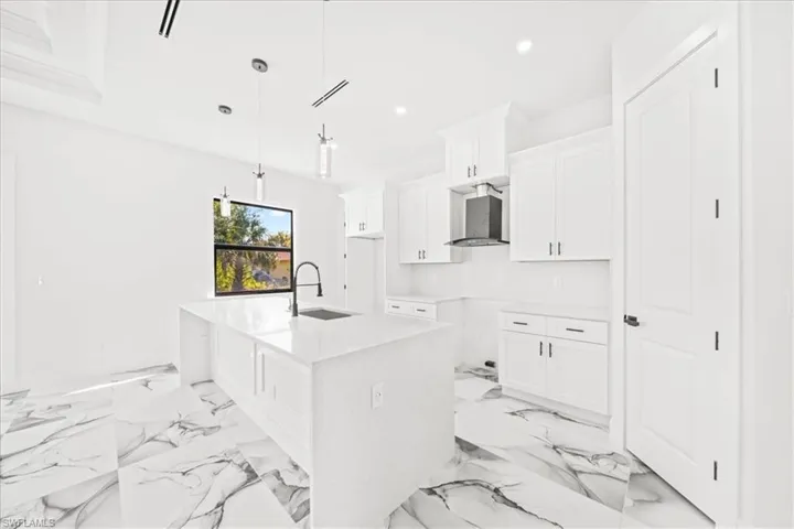 Kitchen featuring a kitchen island with sink, white cabinets, light stone counters, decorative light fixtures, and light marble finish flooring